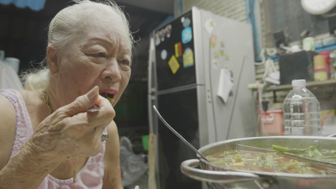 高级亚洲女性在电锅里煮着萝卜、排骨、鱿鱼、玉米、粉丝和猪肉，吃着苏基或沙布。概念：爱、食物、亚洲食物