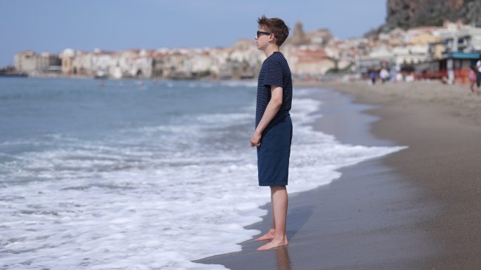 少年男孩站在西西里小镇的海滩上