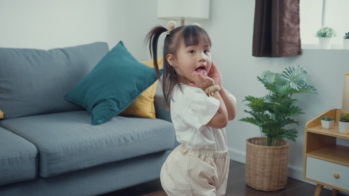 在家里的客厅里，一个蹒跚学步的亚洲女婴对着父母做着傻乎乎的鬼脸。