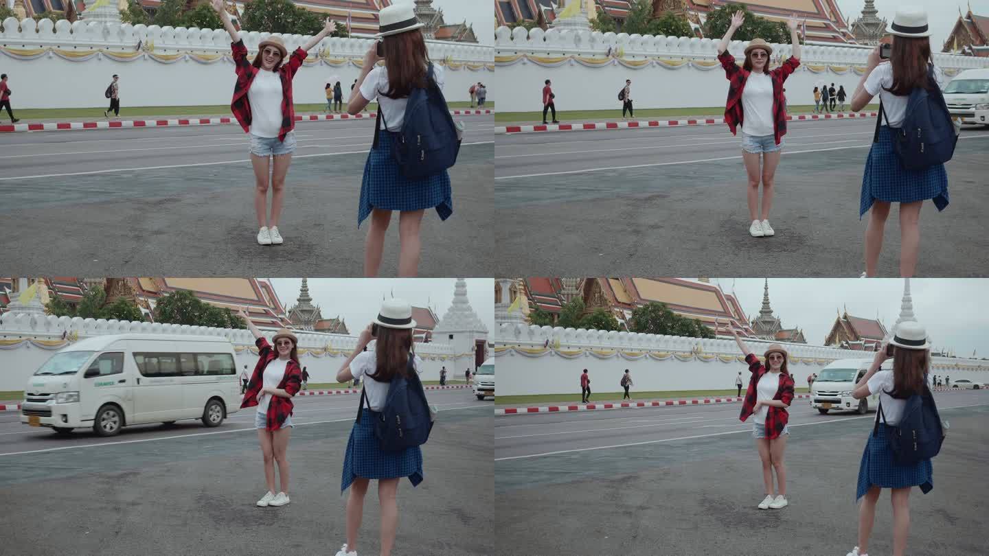 两位美丽的亚洲年轻女游客拍了一张照片，背景是泰国曼谷的大皇宫和湄南河。后视图是意外拍摄的地标/著名地