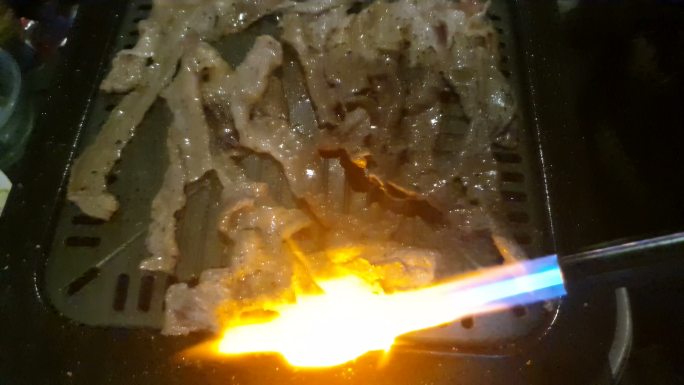 在camfire，厨师手持厨房喷灯在Wagyu牛肉表面燃烧的慢镜头，一名男子在篝火上烧肉的特写镜头