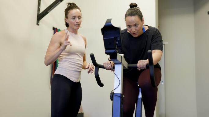 中年女性与健身教练一起在健身自行车上进行有氧运动