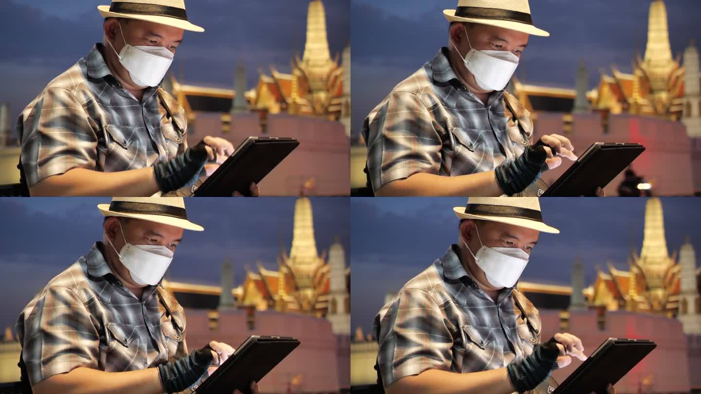 轮椅旅游地标曼谷概念。坐在轮椅上的游客使用手机拍摄大皇宫（Wat Phra Kaew）的照片，并使用