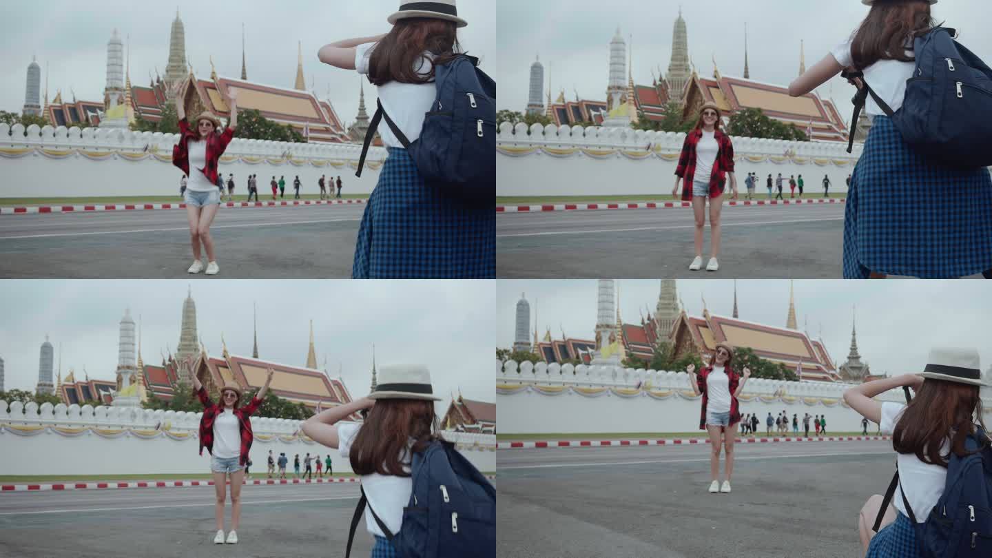 两位美丽的亚洲年轻女游客拍了一张照片，背景是泰国曼谷的大皇宫和湄南河。后视图是意外拍摄的地标/著名地