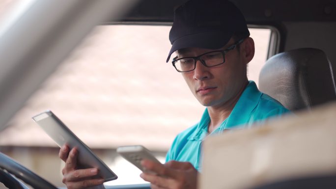亚洲中国成熟男性送货员在送货车内驾驶座用电话与客户沟通