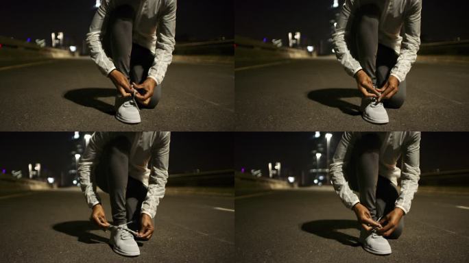 4k视频画面显示，一名无法辨认的女子在夜间在城市道路上跑步前系鞋带