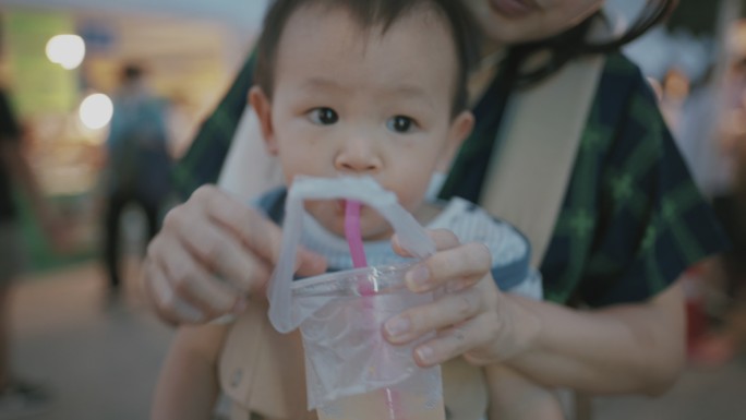 年轻的妈妈在泰国街头食品市场给儿子喂甘蔗汁