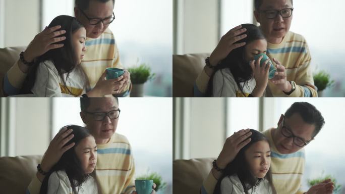 亚洲华人父亲在沙发上为生病的女儿量体温客厅通过数字平板电脑与医生视频通话