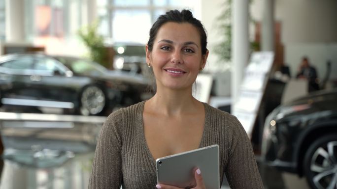 在一家汽车经销店工作的快乐销售女士对着镜头微笑