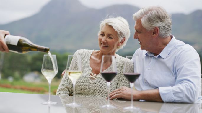 一对退休夫妇在葡萄园里品酒，喝着侍酒师倒的多杯酒。年长的丈夫和妻子在农场里品尝不同的葡萄酒，享受酒杯
