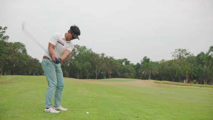 一位亚洲职业男子高尔夫球手在高尔夫球场上进行开球的镜头。