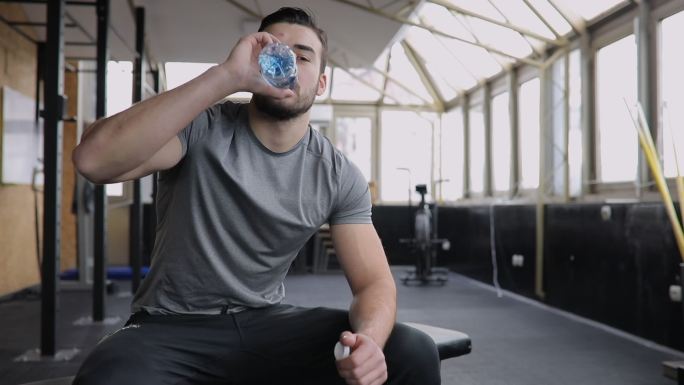 男子训练后饮用水国外健身房强壮男人休息喝