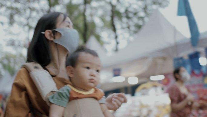 泰国街头食品市场上，亚洲母亲抱着儿子散步