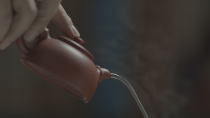 紫砂壶倒出冒着热气的茶水