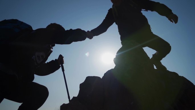 逆光登山剪影手拉手登上山顶攀登顶峰攀登者