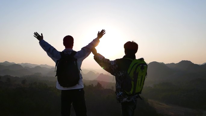 登山成功顶握手庆祝张开双手拥抱夕阳剪影