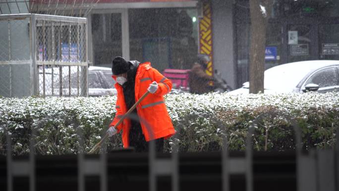 下雪天环卫工人挥动着扫帚扫除积雪