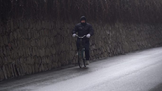 冬季下雪天一位老人骑着自行车经过