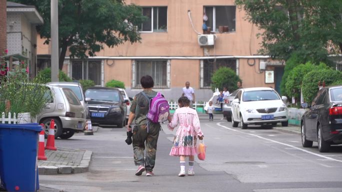 小区内老人接女孩放学手拉手背影