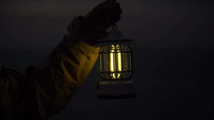 夜晚一个人手里提着一盏灯照亮黑夜站在海边