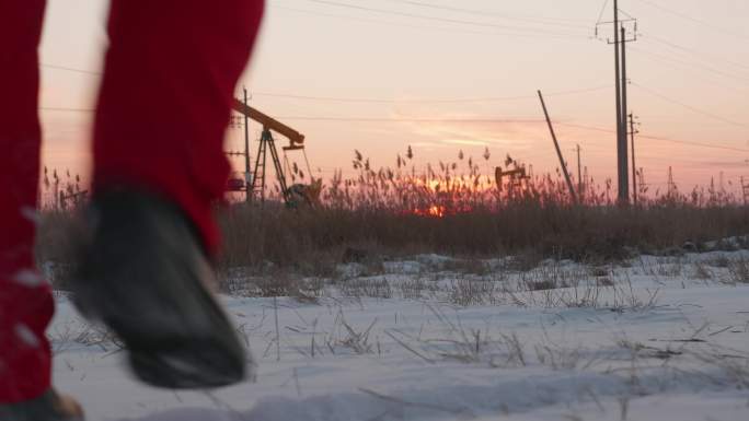 夕阳下抽油机石油工人巡检雪地行走井架剪影