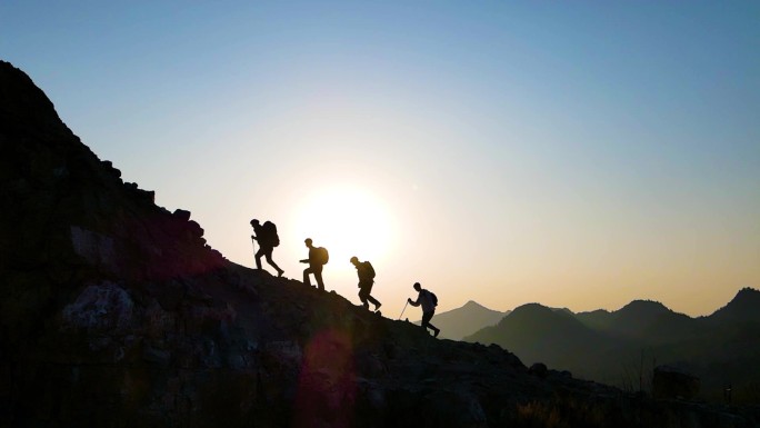 团队逆光登山剪影攀登顶峰冲向山顶眺望远方