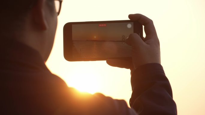 游客拿着手机拍摄夕阳