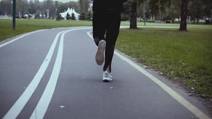 沿着蜿蜒的公园路奔跑的人。后视图。慢动作。穿着白色运动鞋的运动员在安静的小巷上慢跑