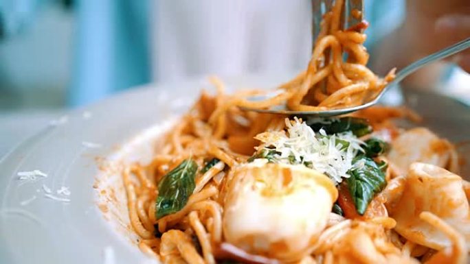 美丽快乐的亚洲女人在餐厅或咖啡馆吃一盘意大利海鲜意大利面，同时微笑着看着食物。