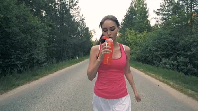 迷人的年轻女士在慢跑时打开瓶子喝酒。健康苗条的年轻女运动员跑步。