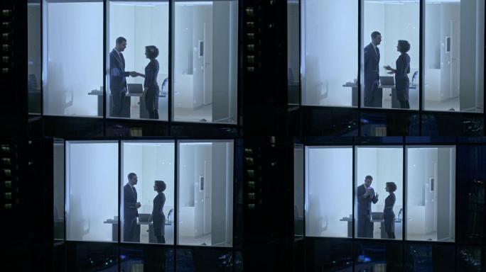 摩天大楼外的航拍镜头: 商人和女商人站在办公室窗户时见面并握手。晚上无人驾驶飞机拍摄商业区和在大城市