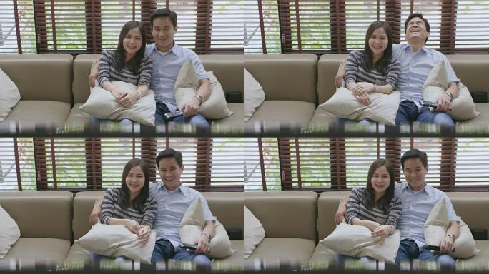 年轻的亚洲夫妇在新房子的沙发上看电视，一起看电影