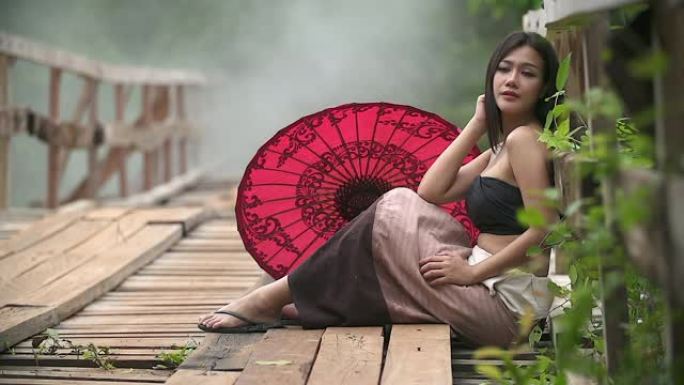 穿着泰国传统服装的亚洲妇女坐在木桥上。