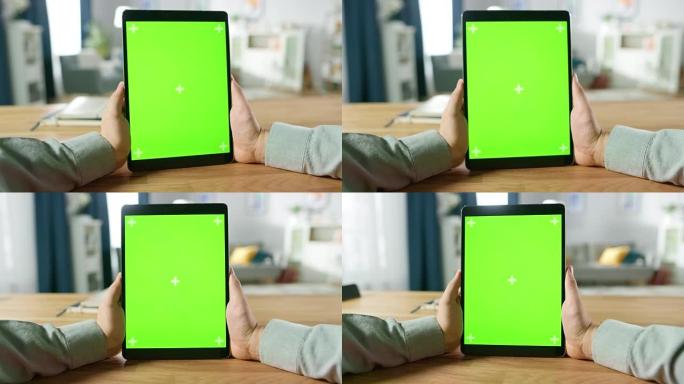 坐在办公桌前，使用绿色模拟屏幕数字平板电脑在肖像模式下拍摄的第一人称照片。背景舒适的客厅。