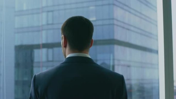 这位体贴的商人穿着西装站在办公室里，正在考虑下一笔大生意，看着窗外。大城市商业区全景窗口视图。