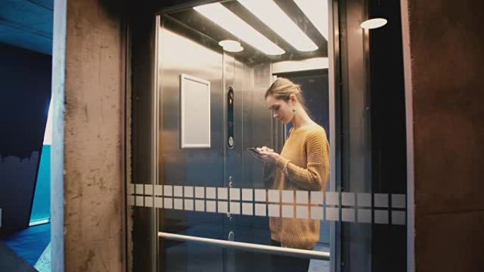 年轻快乐的女孩进入电梯，按下按钮，门关上，她使用智能手机应用程序骑上并微笑着