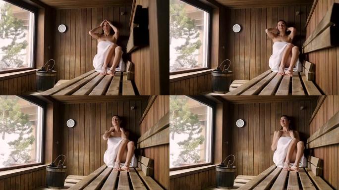 一位穿着白毛巾的美女要洗桑拿: 桑拿是用木头做的，有一个大窗户，可以看到雪。