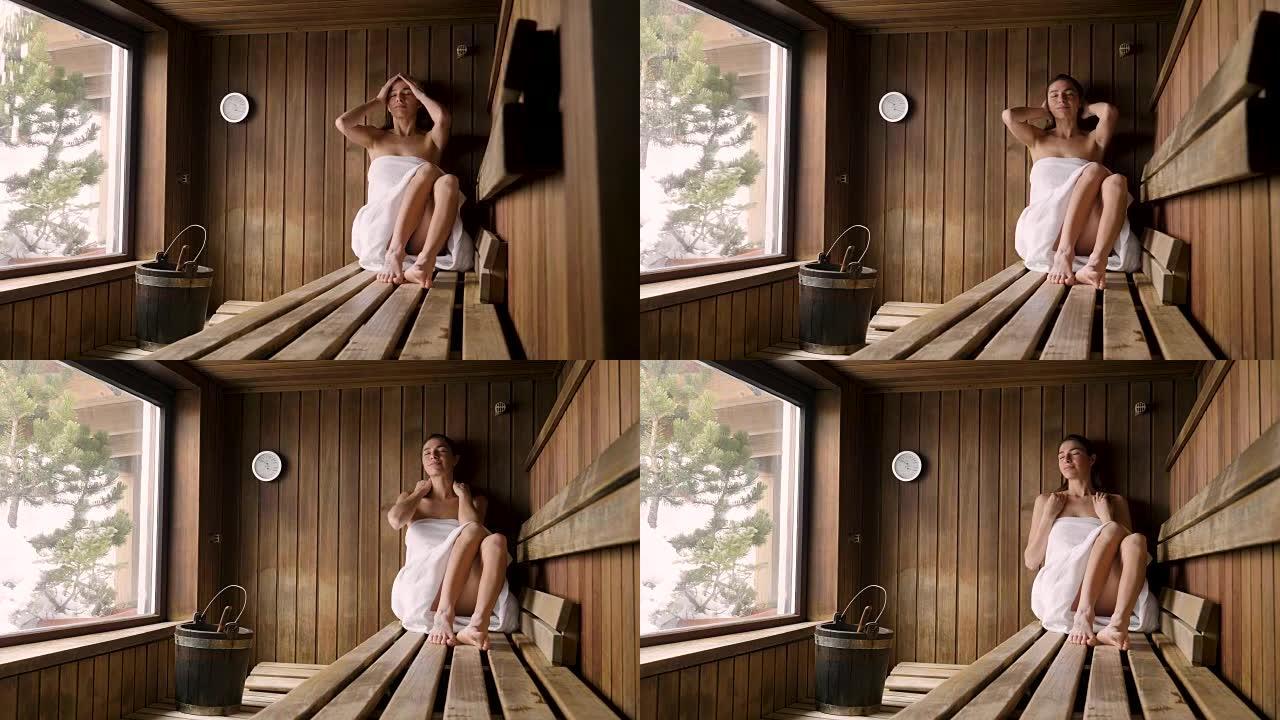 一位穿着白毛巾的美女要洗桑拿: 桑拿是用木头做的，有一个大窗户，可以看到雪。