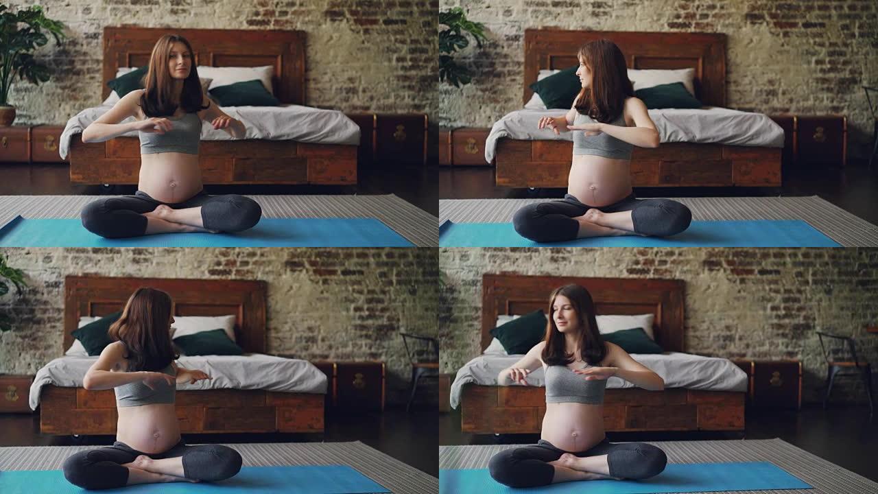 健康怀孕的女孩正在做体育锻炼，坐在卧室地板上的瑜伽垫上，左右转动她的身体。健康的生活方式，现代的内饰