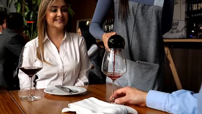 美丽的女服务员在餐厅为一对顾客夫妇提供红酒
