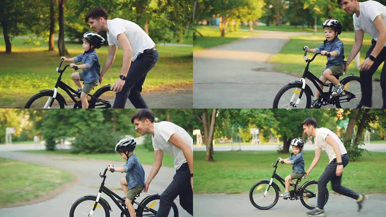 英俊的年轻人慈爱的父亲在夏天教他的小儿子在公园骑自行车，男孩在骑自行车，而爸爸则抱着他跑步。