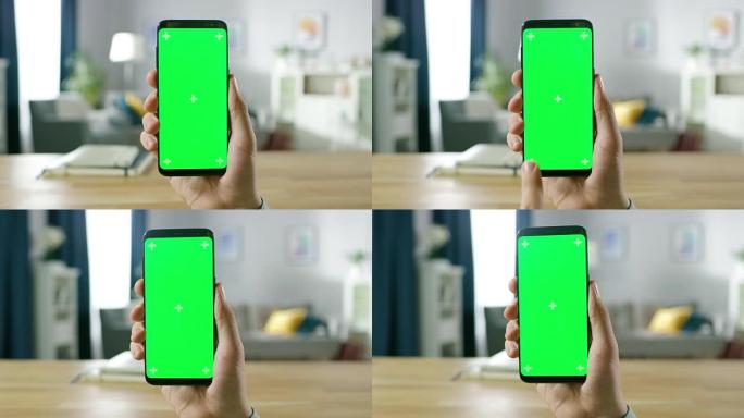 一名男子手持绿色模拟屏幕智能手机并使用触摸屏手势的特写镜头。触摸手机色度键屏幕。背景中舒适的家常氛围