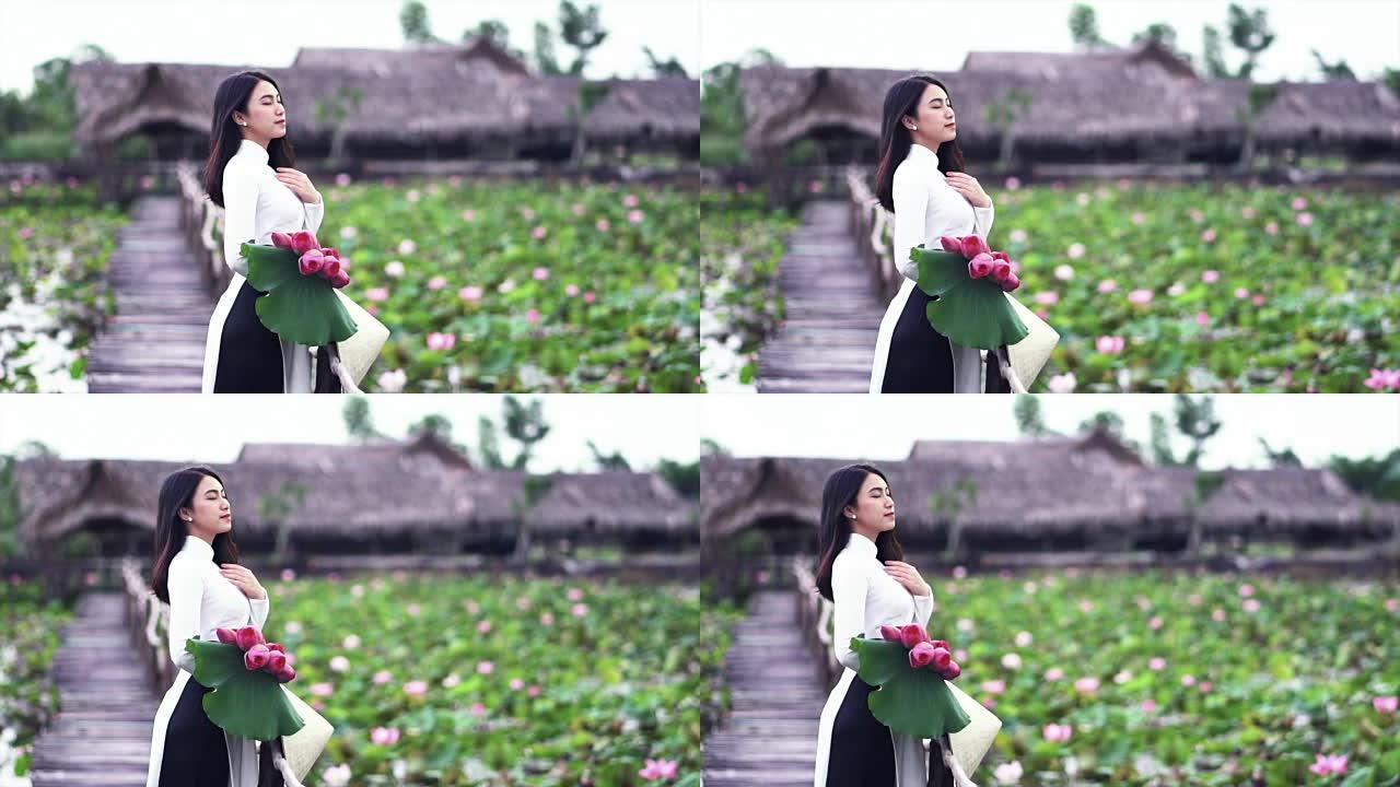 4k慢动作镜头越南美女的肖像拿着粉红色的莲花并在大莲花湖的木桥上获得新鲜空气，越南，亚洲或东南亚旅行