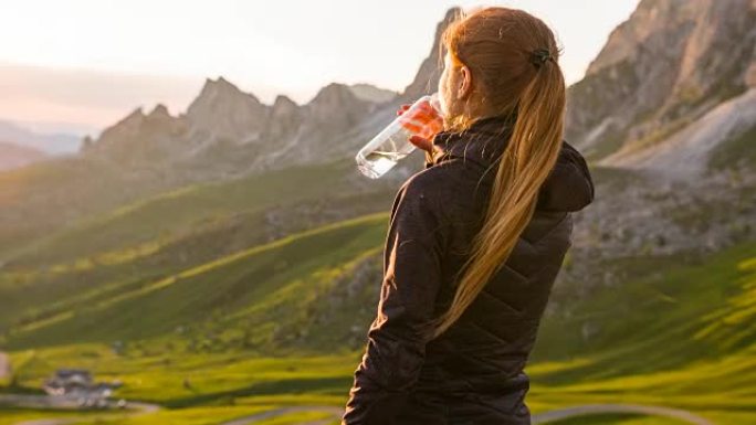 在山坡上的女人被慢慢夕阳照亮，用水瓶喝水