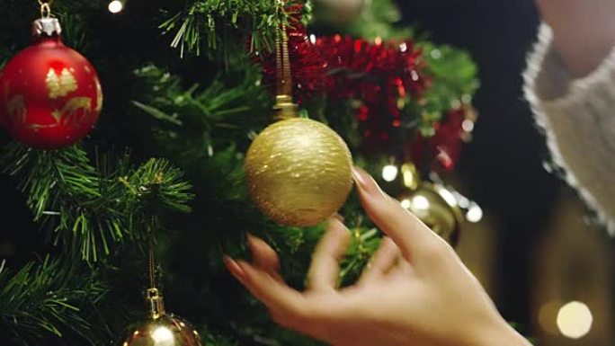 人的手用金色和红色的球装饰圣诞树。等待圣诞节和新年的概念。