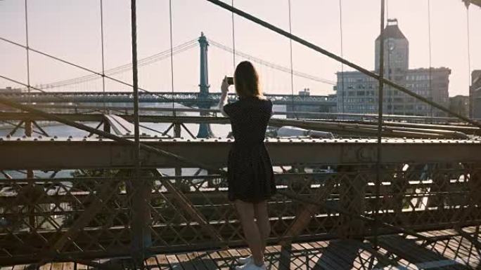 美丽的白人妇女沿着纽约布鲁克林大桥行走，停下来拍摄风景4K的智能手机照片