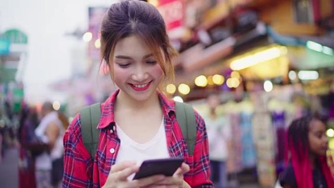 亚洲女性旅游背包客微笑着，使用智能手机独自在曼谷曼谷考山路的城市街道上度假。