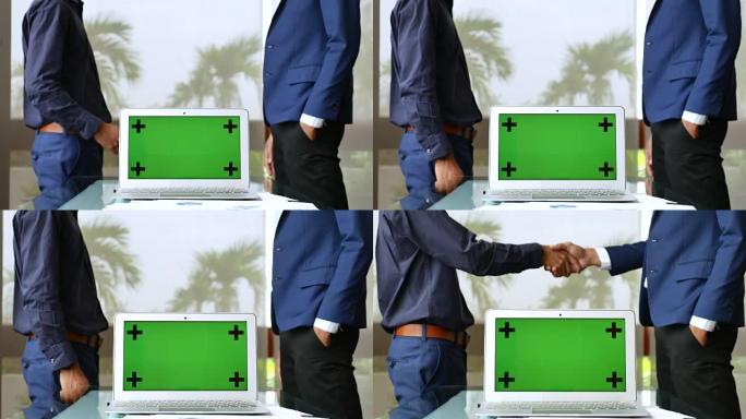 两名商人在绿屏笔记本电脑后面握手