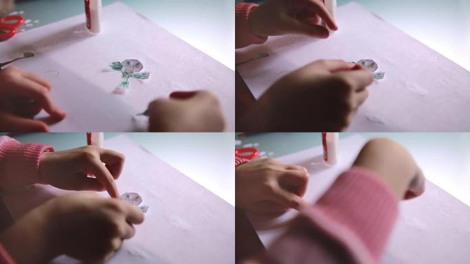 小女孩的手穿着粉红色毛衣的特写镜头，用桌子上的纸和胶水创造了有趣的角色形状