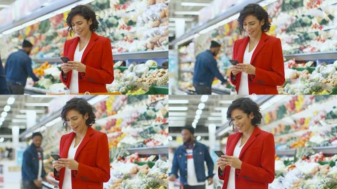 在超市: 美女站在商店的新鲜农产品区时使用智能手机。女人沉浸在网上冲浪在她的手机背景五颜六色的水果和